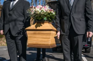 Porteurs de pompes funèbres vêtus de costumes noirs transportant un cercueil en bois orné de fleurs.