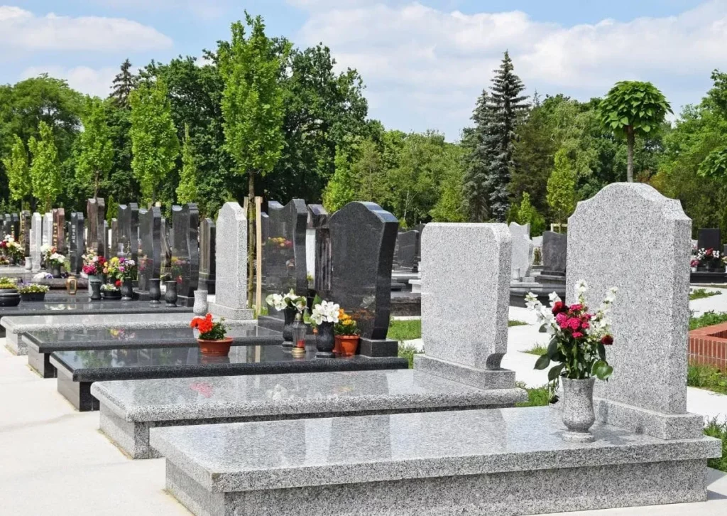 Alignement de tombes en granit dans un cimetière paysager bien entretenu.