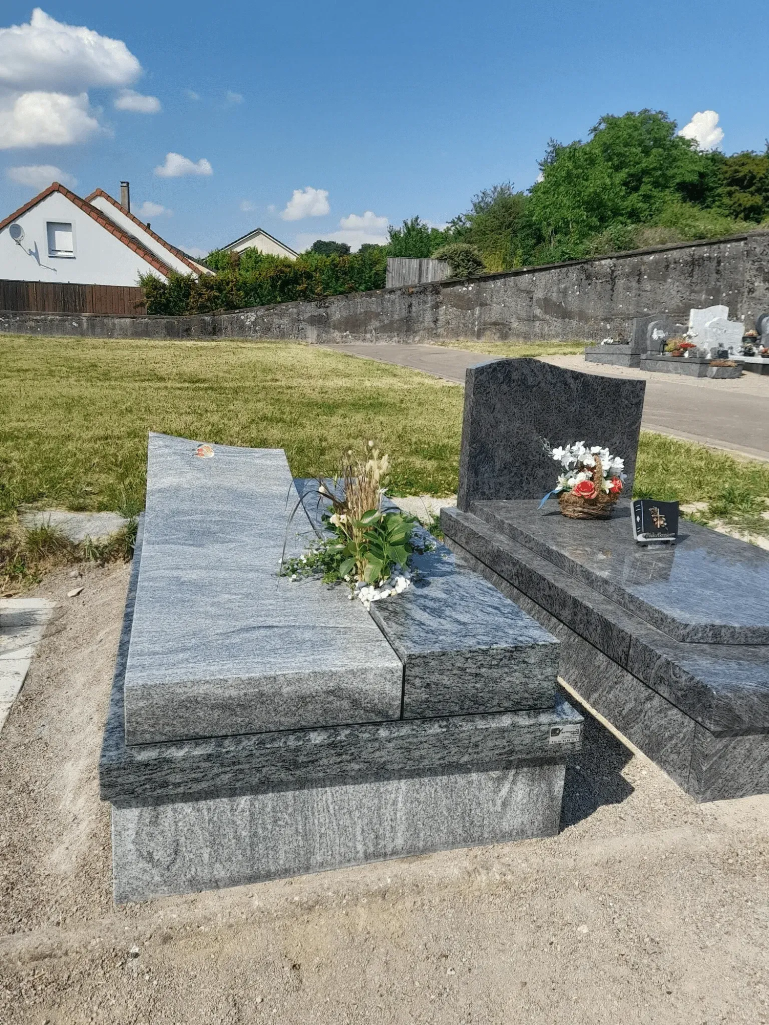 Sépulture en granit gris nuancé surmontée d'une croix dorée gravée.