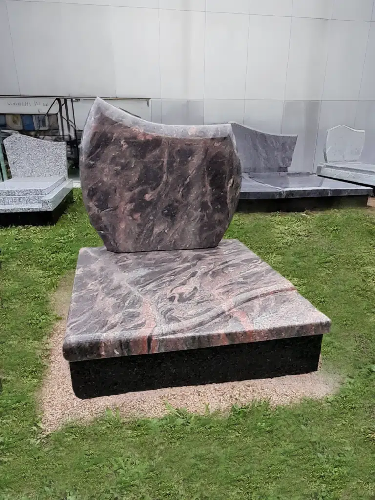 Monument cinéraire en granit rose et noir à la stèle arrondie.